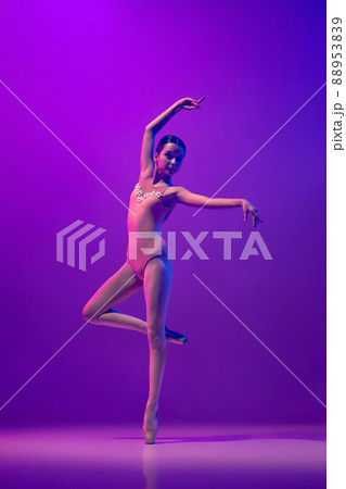 Portrait of young little ballet dancer, teen practicing, dancing isolated on purple background in neon light. Art, grace, beauty, ballet school concept 88953839