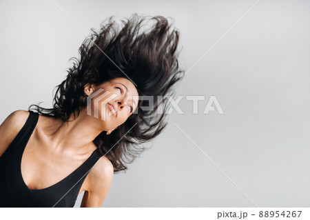 A woman in a black sports T-shirt waves her head with her long hair loose on a gray background 88954267