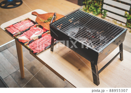 Close up of charcoal grill with raw sliced beef set on wooden table at Outdoor party. 88955307
