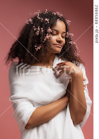 Portrait of young beautiful woman in white bathrobe with small flowers in hair posing isolated over pink studio background 88956862