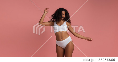 Portrait of cheerful young woman in white underwear posing dancing isolated over pink studio background 88956866