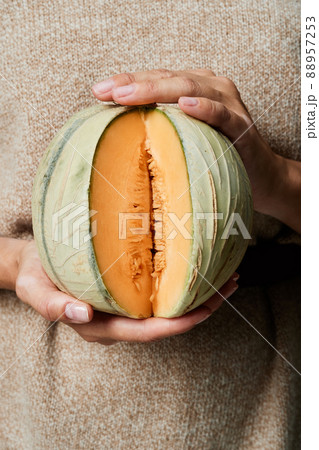 Close-up of unrecognizable woman in beige sweater holding small pumpkin with cut slice Close-up of unrecognizable woman in beige sweater holding small pumpkin with cut slice 88957253