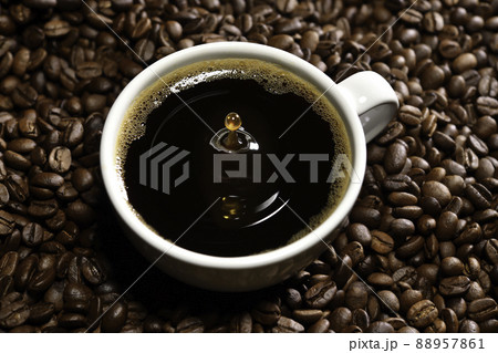 Drop of coffee falling into coffee cup sitting in a pile of freshly roasted coffee beans. Top view Drop of coffee falling into coffee cup sitting in a pile of freshly roasted coffee beans. Top view 88957861