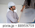 Architect in white helmets reviewing blueprints at a construction site. 88959759