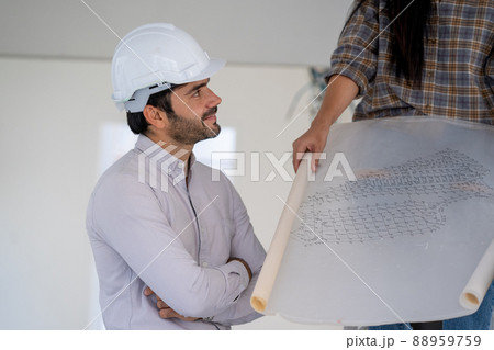 Architect in white helmets reviewing blueprints at a construction site. 88959759