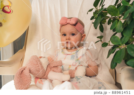 serious little girl in beautiful dress sits on an armchair and looks at the camera serious little girl in beautiful dress sits on an armchair and looks at the camera 88961451
