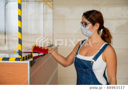 Woman in mask giving her passport at the airport check-in counter. 88963537