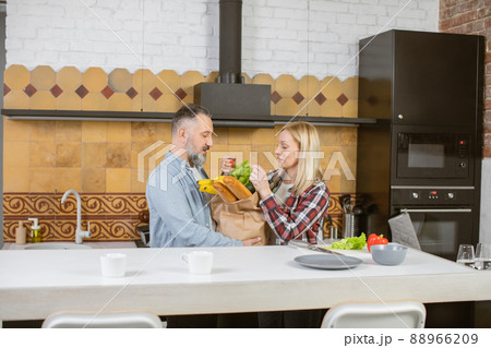 Mature married couple unpacking grocery bag on kitchen Mature married couple unpacking grocery bag on kitchen 88966209