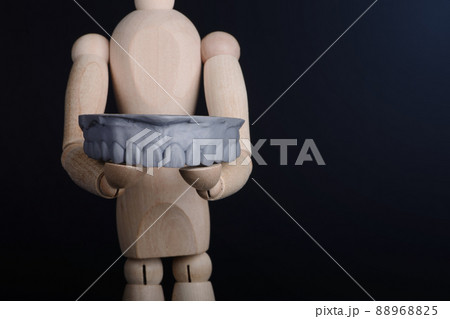 Human wooden figure holds in hands a dental upper jaw model printed on 3d printer on a black background. Human wooden figure holds in hands a dental upper jaw model printed on 3d printer on a black background. 88968825