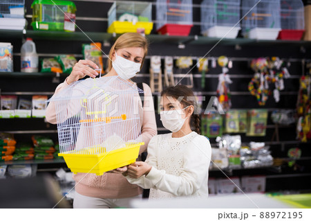 Mother with her daughter in masks choosing bird cage Mother with her daughter in masks choosing bird cage 88972195