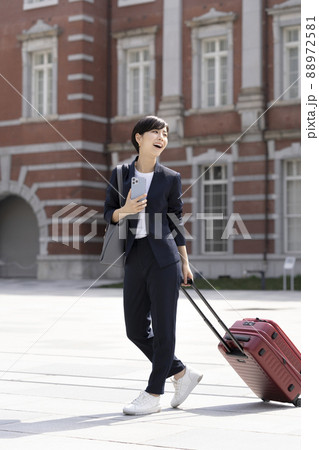キャリーバッグを引いて歩くスマホを持ったビジネスウーマン 88972581