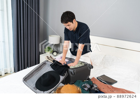 stressed man having problem with packing clothes into a suitcase on bed, holiday travel concept stressed man having problem with packing clothes into a suitcase on bed, holiday travel concept 88972624