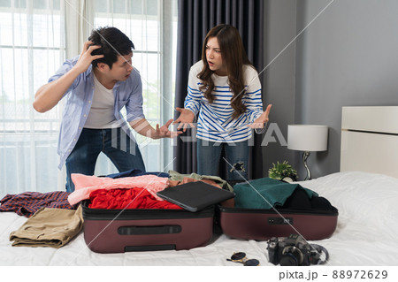 stressed couple having problem with packing clothes into a suitcase on bed at home, holiday travel concept stressed couple having problem with packing clothes into a suitcase on bed at home, holiday travel concept 88972629
