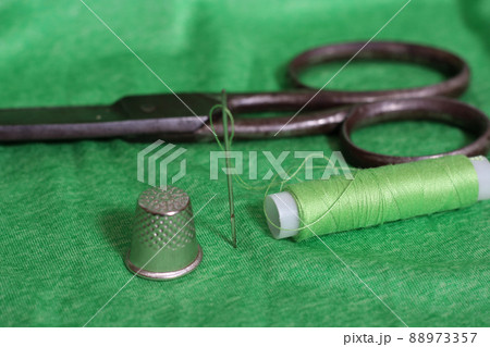 Spool of Green Thread, Thimble and Needle on Green Fabric 88973357