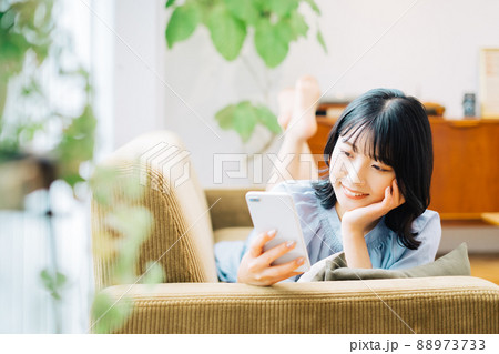 ソファに寝転がってスマホを持つ女性 88973733