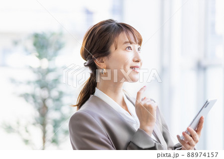 スマホを持って明るい窓辺に立つビジネスウーマン 88974157