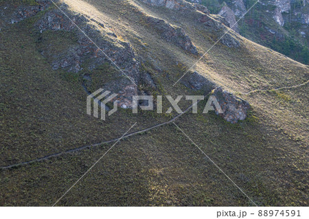 Hillside is crossed by hiking trail. Travel in mountains. Cross country running. Granite stones and cliffs protrude on slope. 88974591