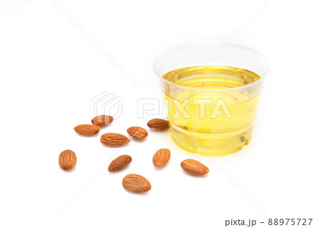 Yellow almond oil in a clear bowl and several almonds on a white background Yellow almond oil in a clear bowl and several almonds on a white background 88975727
