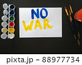 Man paints poster for rally with the slogan NO TO WAR. With brush and paints, he prints colorful bright letters on sheet. Person's requirement. Poster with call, rally, picket, march, protest, action 88977734