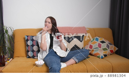 A pregnant girl drinks alcohol on the couch and eats marshmallows. A young woman is pregnant. Early pregnancy A pregnant girl drinks alcohol on the couch and eats marshmallows. A young woman is pregnant. Early pregnancy 88981304