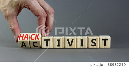 Activist or hacktivist symbol. Businessman turns wooden cubes and changes the word Activist to Hacktivist. Beautiful grey table grey background, copy space. Business activist or hacktivist concept. 88982250