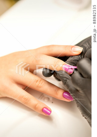 Professional manicure. A manicurist is painting the female nails of a client with purple nail polish in a beauty salon, close up. Beauty industry concept Professional manicure. A manicurist is painting the female nails of a client with purple nail polish in a beauty salon, close up. Beauty industry concept 88982535