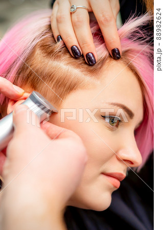 Hairdresser shaves female temple with pink hair by electric shaver in a hairdresser salon, close up 88982624