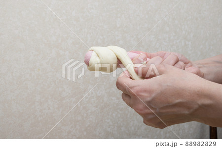 Women's hands wrap sausages in dough in the home kitchen. The process of preparing a hot dog close-up. Women's hands wrap sausages in dough in the home kitchen. The process of preparing a hot dog close-up. 88982829
