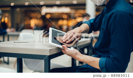 man in protective mask wiping the screen of a digital tablet with antiseptic 88983011