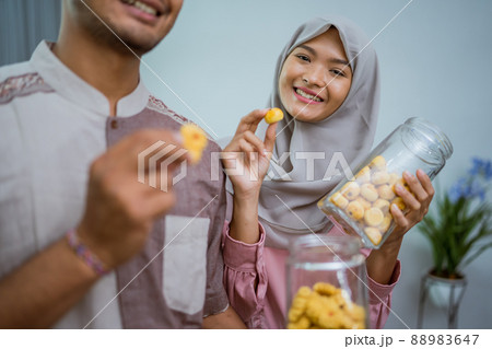 muslim couple holding idul fitri snack smiling to camera 88983647