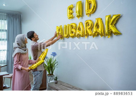 muslim couple decorating their house with eid mubarak text on the wall muslim couple decorating their house with eid mubarak text on the wall 88983653