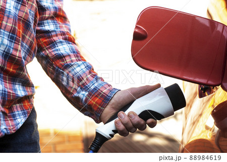 Male model stands by an electric car and holds a charging plug Male model stands by an electric car and holds a charging plug 88984619