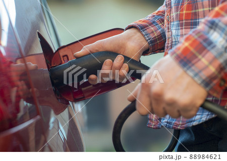 Male model stands by an electric car and holds a charging plug Male model stands by an electric car and holds a charging plug 88984621