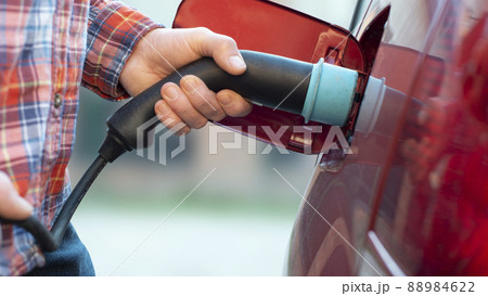 Male model stands by an electric car and holds a charging plug 88984622