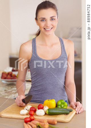 She enjoys food and loves cooking. Portrait of a beautiful young woman chopping up vegetables in the kitchen. 88984752