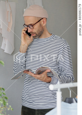 male fashion designer or fashion designer flips through a magazine and talks on the phone with a client. an adult business man is working in his office 88986179