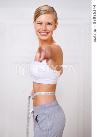 Ive reached my goal weight and so can you. A portrait of a beautiful young woman measuring her waist and pointing. Ive reached my goal weight and so can you. A portrait of a beautiful young woman measuring her waist and pointing. 88986344