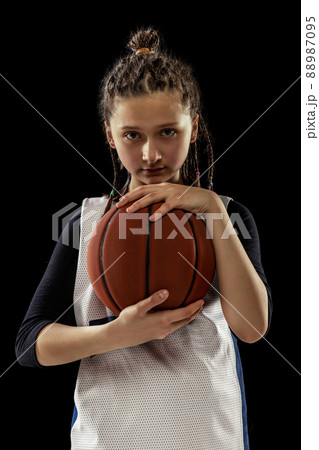 Portrait of teen girl, concentrated basketball player in uniform posing isolated over black studio background Portrait of teen girl, concentrated basketball player in uniform posing isolated over black studio background 88987095