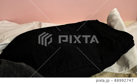 Jeans of different colors are scattered on a pink background. Gray, black, light, white jeans are on the table. Background with jeans 88992747