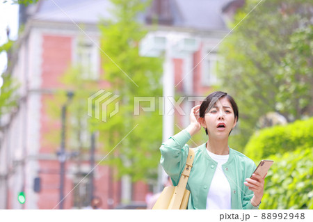 スマホを持ち困った表情で顔を上げた女性1 スマホを持ち困った表情で顔を上げた女性1 88992948