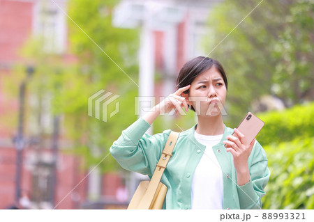 スマホを持ち口をとがらせて困った表情の女性1 スマホを持ち口をとがらせて困った表情の女性1 88993321