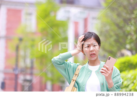 スマホを持ち頭を抱え困った表情の女性1 スマホを持ち頭を抱え困った表情の女性1 88994238