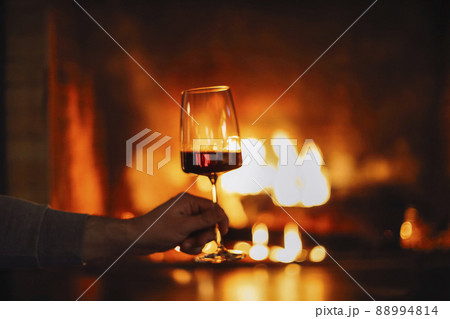 Man having red wine by the fireplace. Close up of man holding and drinking red wine glass 88994814