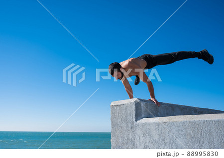 Shirtless man doing a handstand on a parapet by the sea. Shirtless man doing a handstand on a parapet by the sea. 88995830