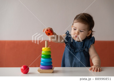 Baby girl playing with wooden colourful toy pyramid at home. Baby girl playing with wooden colourful toy pyramid at home. 88996851