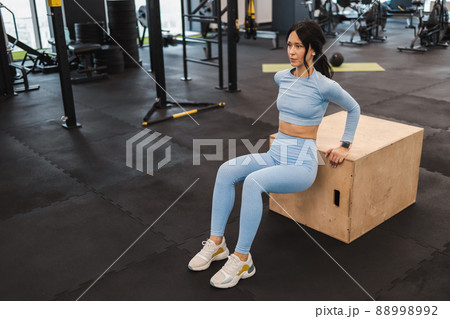 Pretty woman doing reverse push-up on triceps on crossfit box in gym 88998992
