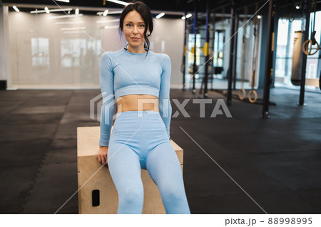 Woman in blue sportswear doing triceps exercises on wooden crossfit jump box at gym 88998995