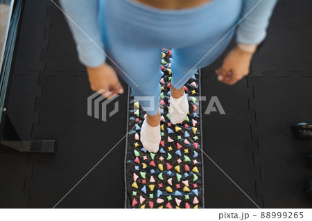 Acupuncture points of the foot stimulation. Woman stand on orthopedic foot massage mat. Massage rug with colorful stones Acupuncture points of the foot stimulation. Woman stand on orthopedic foot massage mat. Massage rug with colorful stones 88999265