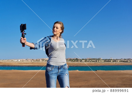 Middle-aged woman recording video on smartphone with outdoor on seashore Middle-aged woman recording video on smartphone with outdoor on seashore 88999691