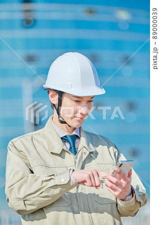 ビルの前でスマホを操作する作業服姿の若い男性 ビルの前でスマホを操作する作業服姿の若い男性 89000039